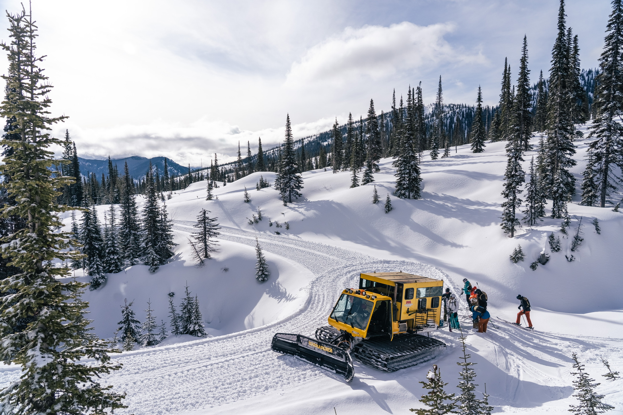 Yellow snowcat and riders among snow-covered trees