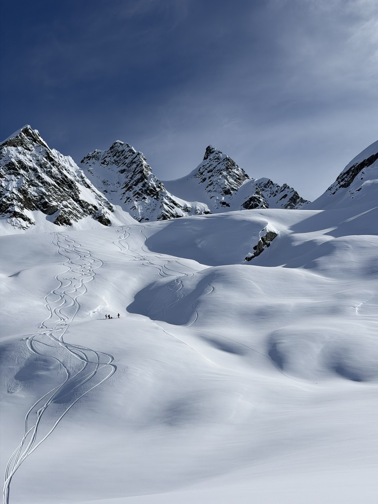 Ski tracks winding across a broad mountain snowfield